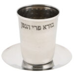 כוס קידוש מהודרת מכסף חלקה עם הכיתוב "בורא פרי הגפן", בגובה 8 ס"מ, מונחת על צלוחית כסף תואמת.